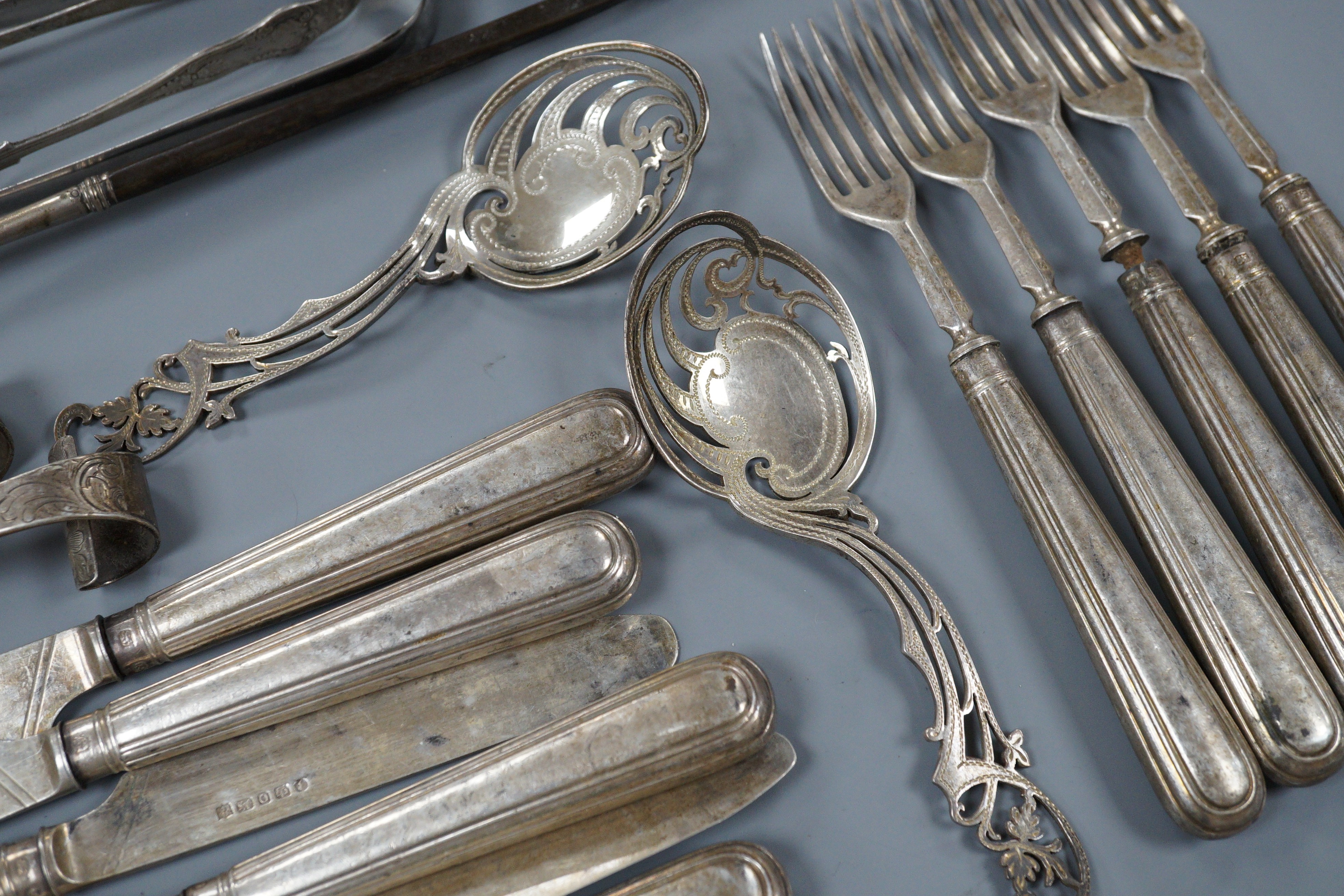 A pair of Victorian silver scrolling knife rests, George Adams, London, 1859, 10.4cm, a pair of pierced silver spoons, two pairs of silver sugar tongs, a part set of Victorian silver dessert eaters(6 & 5), a toddy ladle